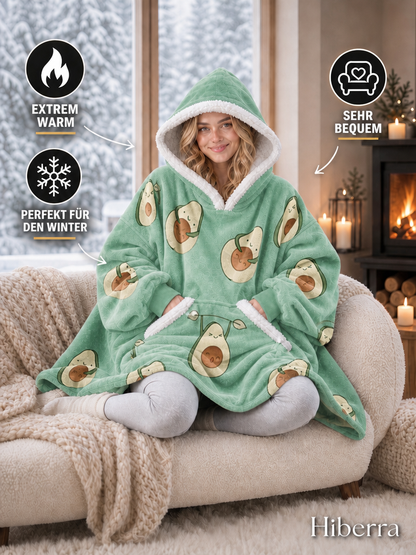 Frau im Hiberra Kuschelhoodie in Avocado-Print auf dem Sofa – extra warm, sehr bequem, perfekt für den Winter – Farbe Avocado-Print