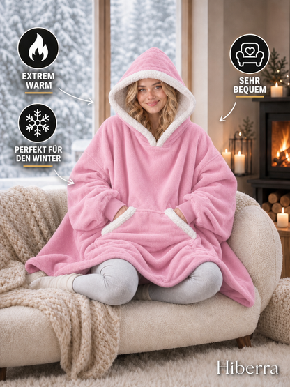 Frau im rosa Hiberra Kuschelhoodie auf dem Sofa – extra warm, sehr bequem, perfekt für den Winter – Farbe Rosa