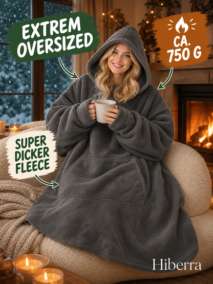 Frau in der dunkelgrauen Hiberra Hoodie-Decke mit Tee am Kamin, ca. 750 g – Farbe Dunkelgrau