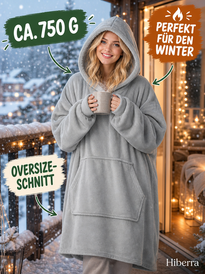 Frau in der hellgrauen Hiberra Hoodie-Decke steht mit Tasse auf dem Balkon im Schnee, ca. 750 g – Farbe Hellgrau