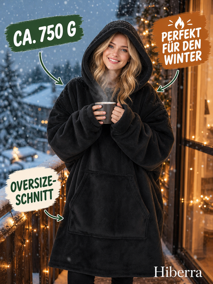 Frau in der schwarzen Hiberra Hoodie-Decke steht mit Tasse auf dem Balkon im Schnee, ca. 750 g – Farbe Schwarz