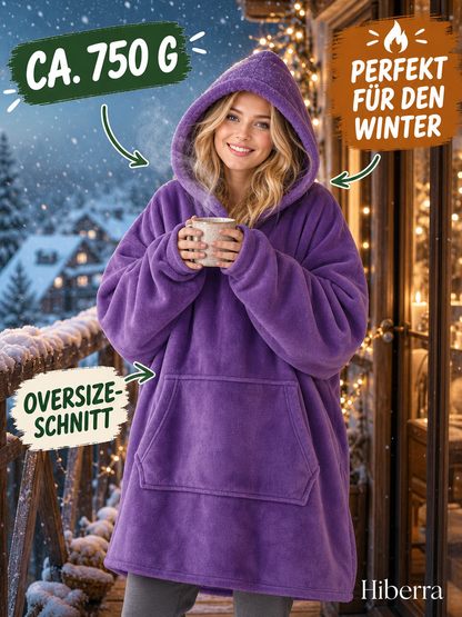 Frau in der lila Hiberra Hoodie-Decke steht mit Tasse auf dem Balkon im Schnee, ca. 750 g – Farbe Lila