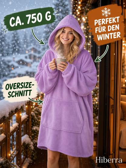 Frau in der fliederfarbenen Hiberra Hoodie-Decke steht mit Tasse auf dem Balkon im Schnee, ca. 750 g – Farbe Flieder
