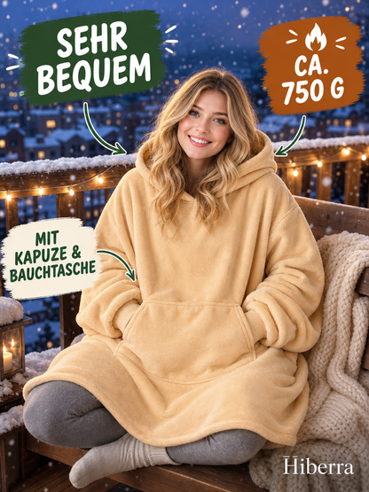 Frau in der beigegelben Hiberra Hoodie-Decke sitzt auf dem verschneiten Balkon, ca. 750 g – Farbe Beigegelb