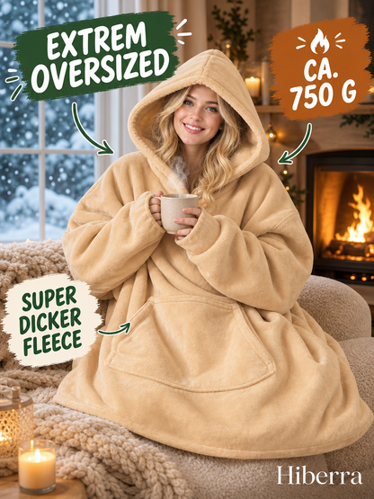 Frau in der beigegelben Hiberra Hoodie-Decke mit Tee am Kamin, ca. 750 g – Farbe Beigegelb