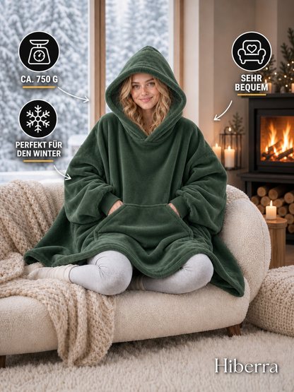 Frau in der dunkelgrünen Hiberra Hoodie-Decke auf dem Sofa, ca. 750 g – Farbe Dunkelgrün