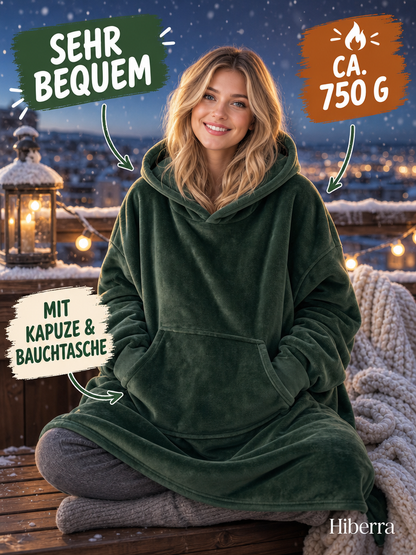 Frau in der dunkelgrünen Hiberra Hoodie-Decke sitzt auf dem verschneiten Balkon, ca. 750 g – Farbe Dunkelgrün