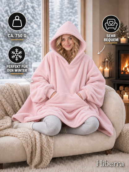 Frau in der puderrosa Hiberra Hoodie-Decke auf dem Sofa, ca. 750 g – Farbe Puderrosa