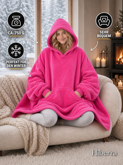 Frau in der pinken Hiberra Hoodie-Decke auf dem Sofa, ca. 750 g – Farbe Pink